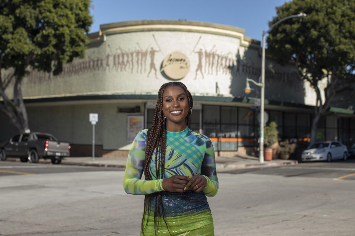 Issa Rae poses for a portrait in a dress of greens, blues and purple.