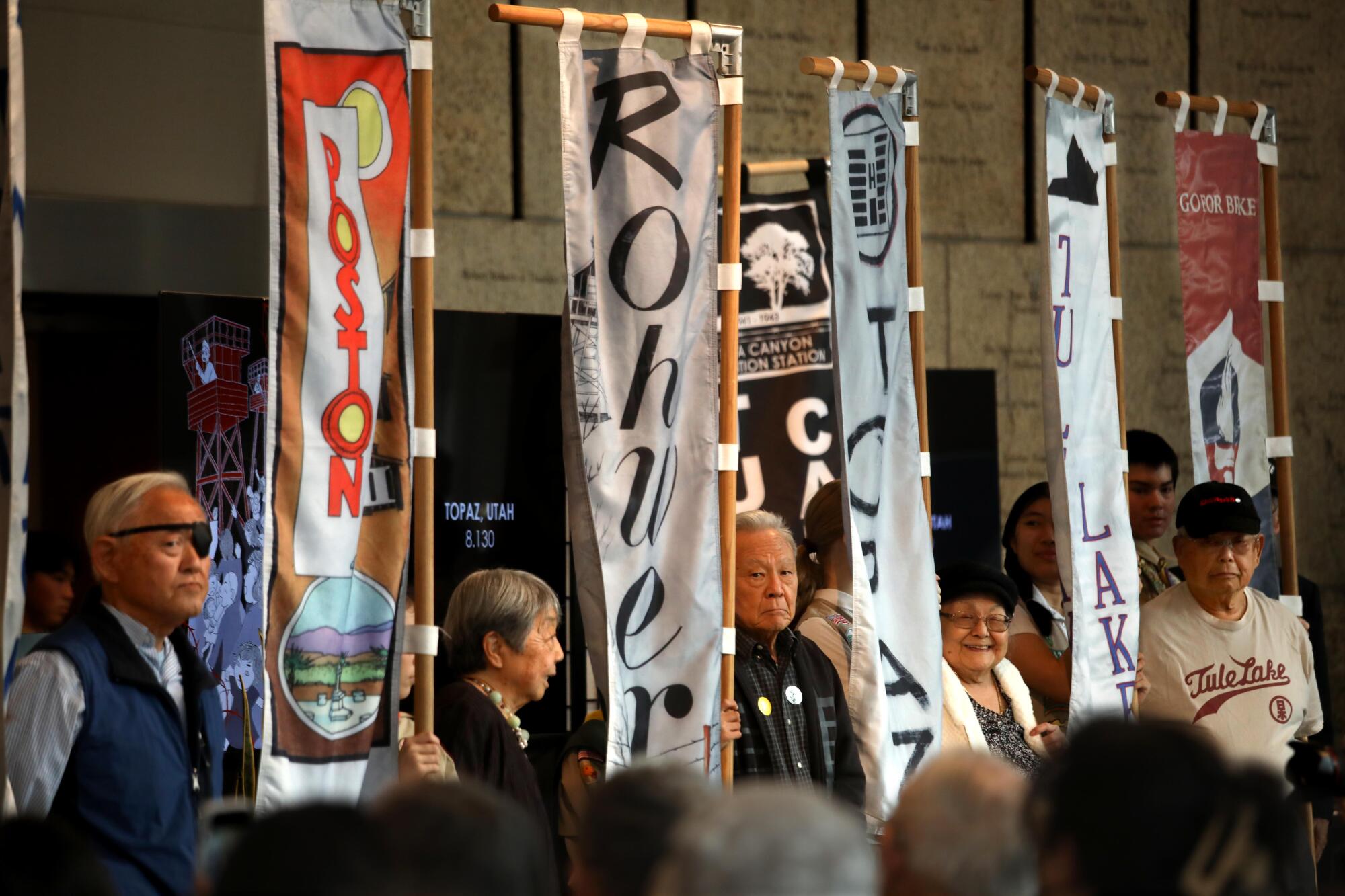 Incarceration camp flags hang at the Japanese American National Museum while people stand next to them.