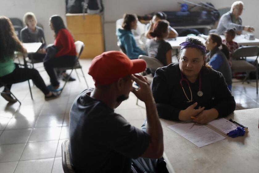 In this Dec. 14, 2019, photo, Dr. Psyche Calderon, right, works with a patient in a shelter for migrants in Tijuana, Mexico. Calderon is part of a movement of health professionals and medical students from both sides of the U.S.-Mexico border that is quietly battling to keep asylum seekers healthy and safe while their lives remain in flux. (AP Photo/Gregory Bull)