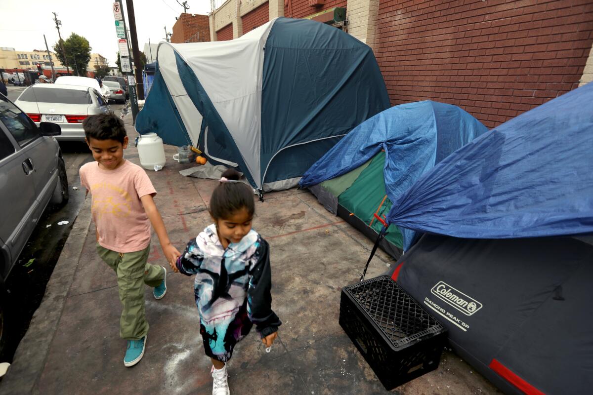 Migrant children Celeste, 5, right, and her brother Dylan, 8, from Columbia, walk by homeless encampments.