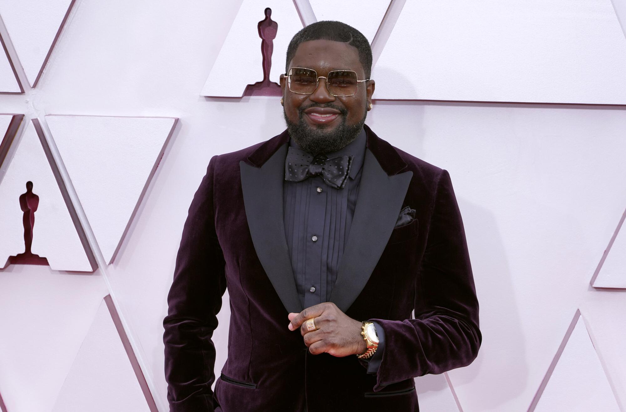 Lil Rel Howery arrives at the Oscars in a black shirt and bow tie and purple jacket.