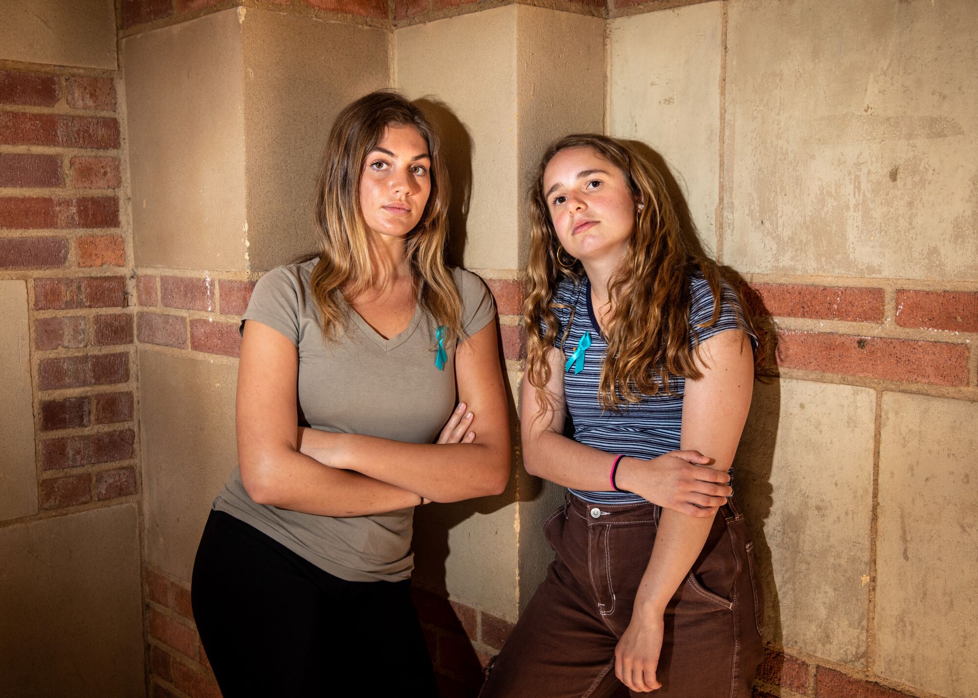 Two students stand side by side, leaning against the stone wall behind them, looking into the camera.