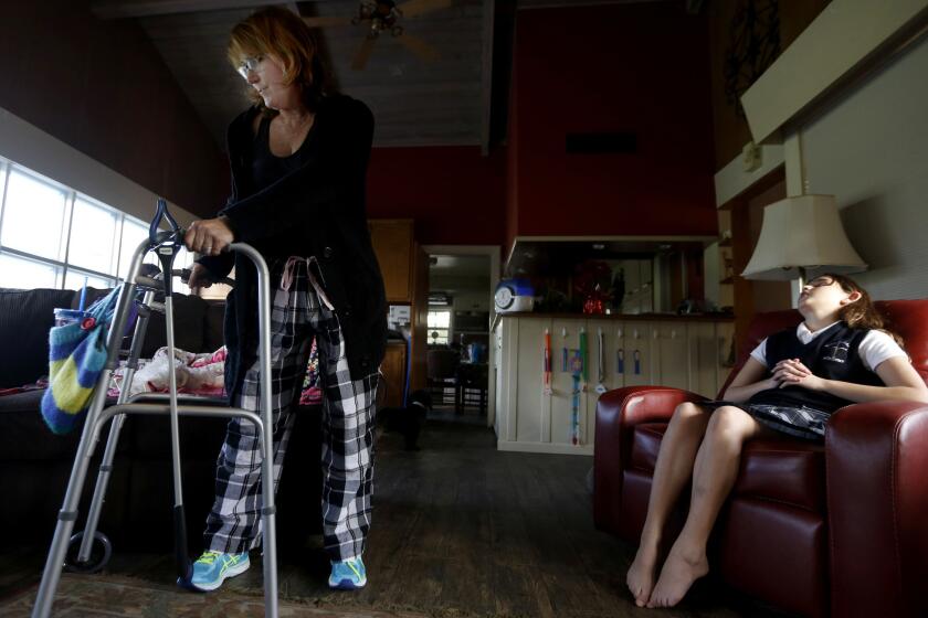 Julie Swann-Paez, shot in the pelvis in the Dec. 2 attack at the Inland Regional Center, uses a walker to move around her living room. She takes Tylenol to endure the pain and a muscle relaxant to sleep through the night. At right is her daughter Ellie, 11.