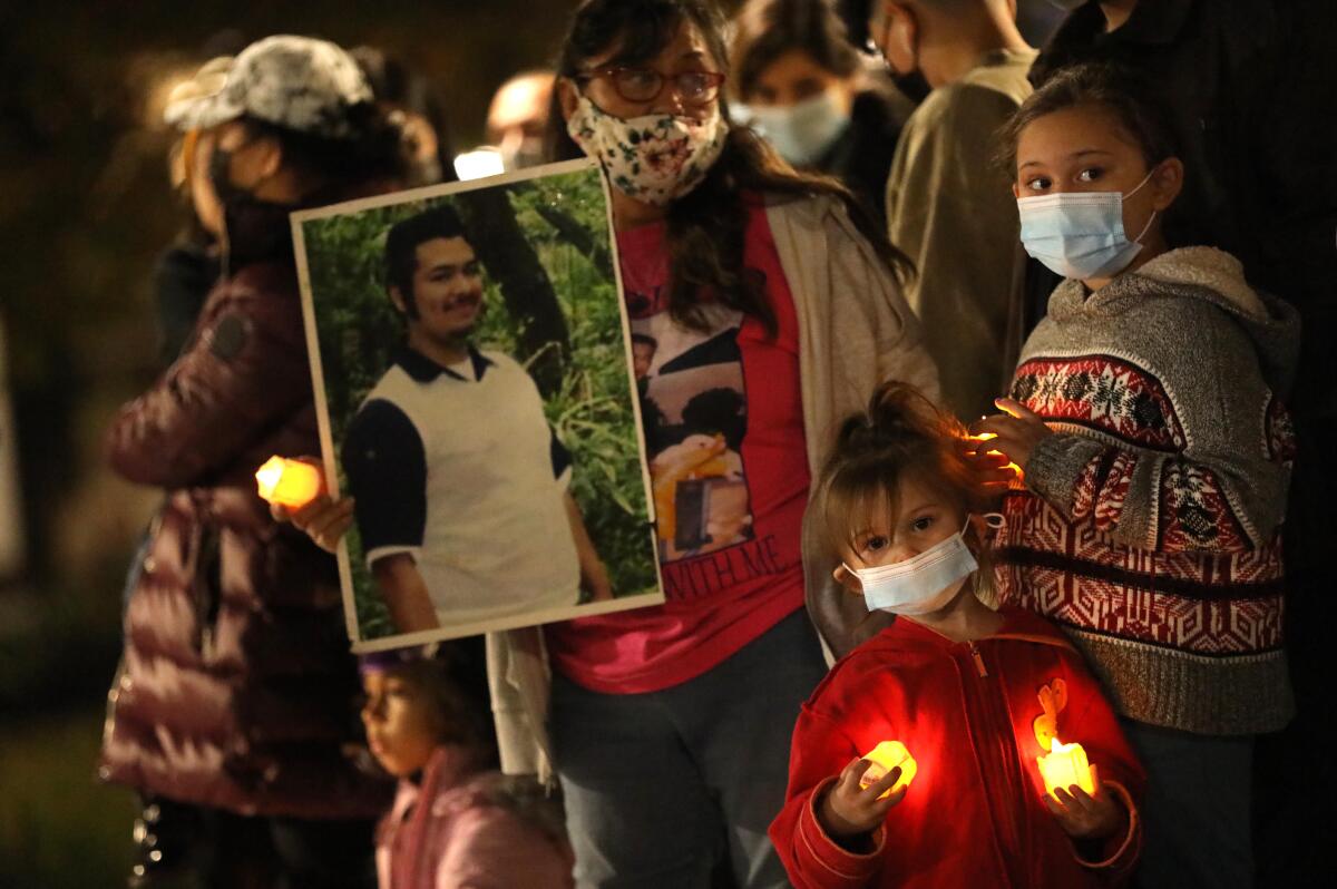 A woman surrounded by three children holds a poster-size photo of a man.