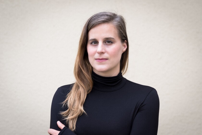 A woman in a black turtleneck looks into the camera