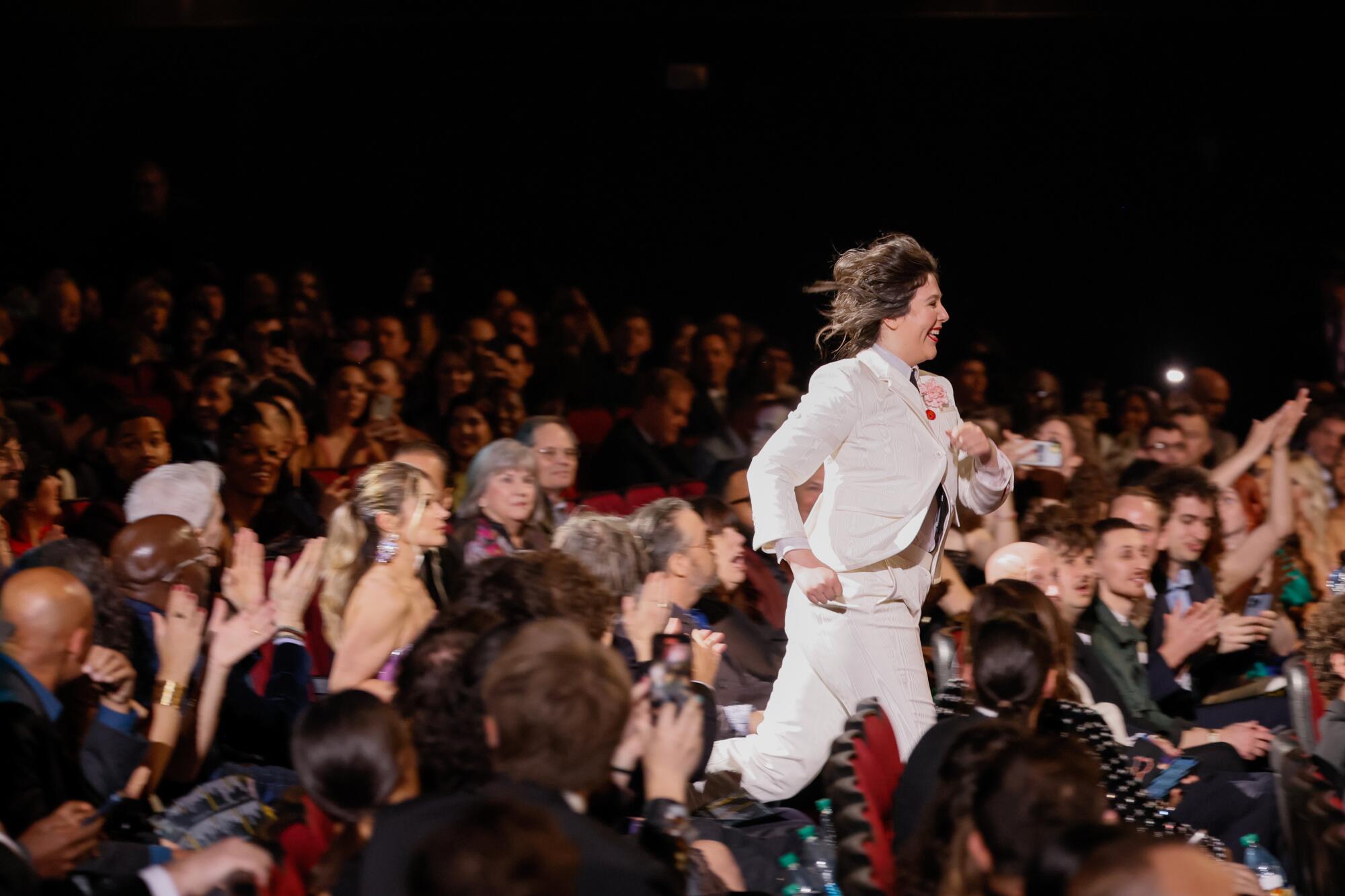 Lucy Dacus of Boygenius wears a white suit and runs up the aisle to accept a Grammy award