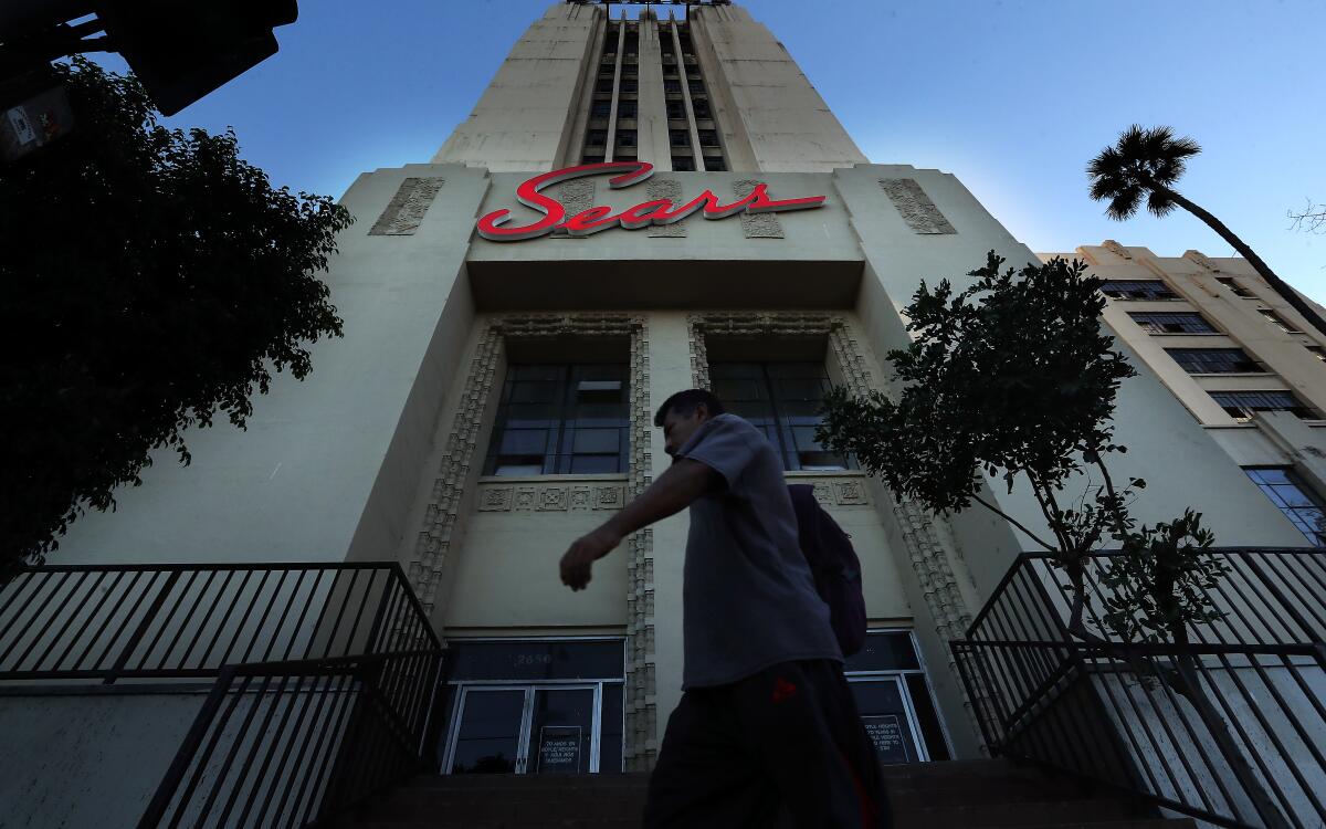 A person walks an Art Deco tower with a neon "Sears" sign.