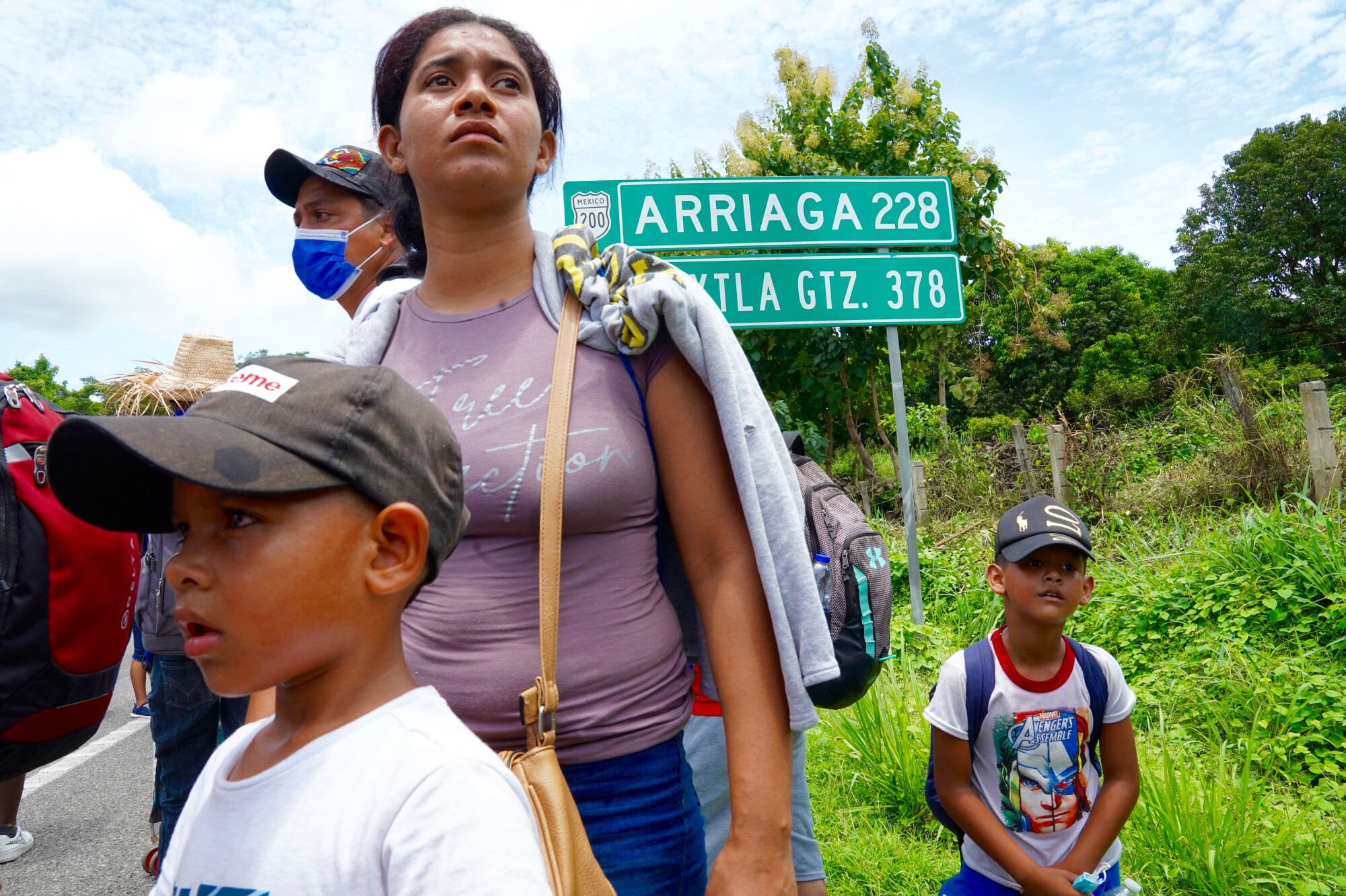 A woman and children walk on the side of a road.  