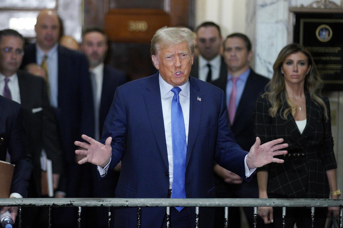 Former President Trump holds his hands out in front of him while people stand behind him.