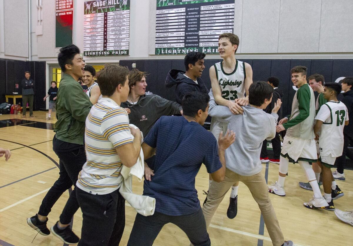Sage Hill School's Jack Strohman (23) is mobbed by his schoolmates after he hit a game-winning shot at the buzzer to beat North Hollywood Oakwood 63-62 in a CIF State Southern California Regional Division V playoff opener on Tuesday.