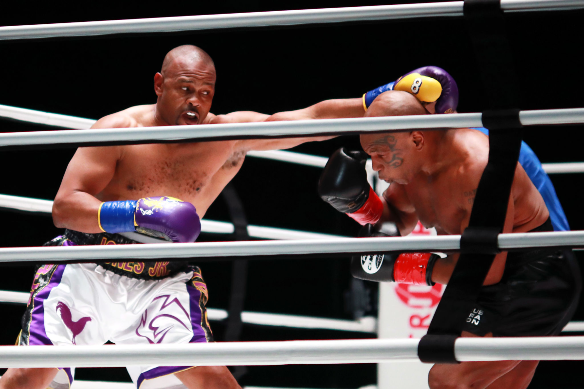 One boxer holds out his left arm as another boxer bends down. 