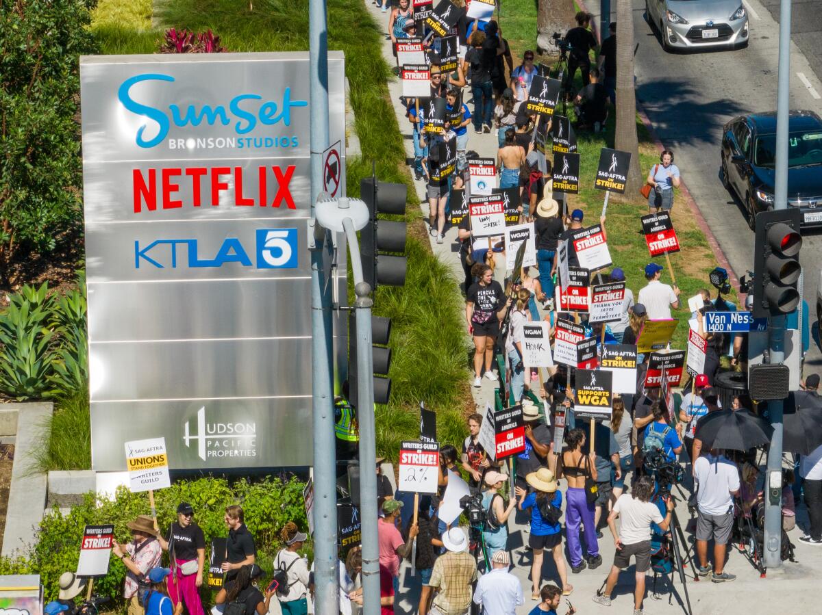 An overhead view shows a Hollywood street corner packed with people carrying picket signs