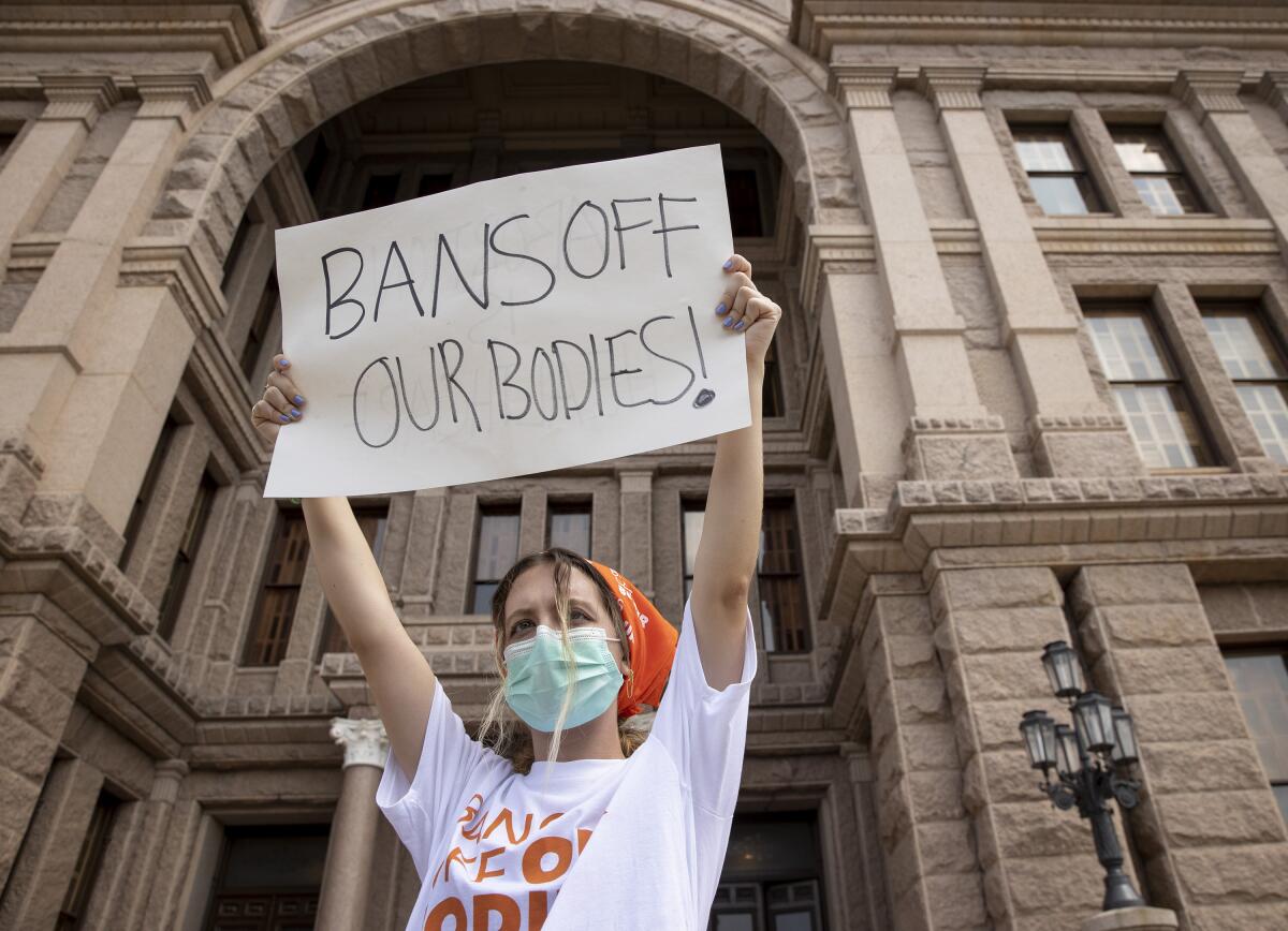 A masked person holds a sign reading 'bans off our bodies' outside the state Capitol in Austin, Texas