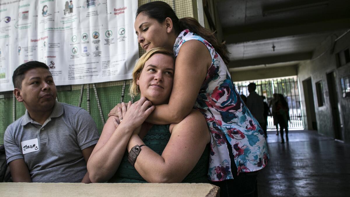 Attorney Nora Phillips, center, is hugged by attorney Tania Vargas as Jorge Gutierrez looks on during an immigration clinic in Tijuana.