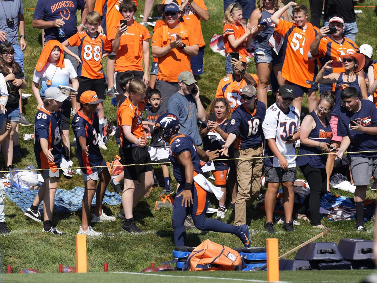 Russell Wilson, quarterback de los Broncos de Denver, corre cerca de los fanáticos del equipo