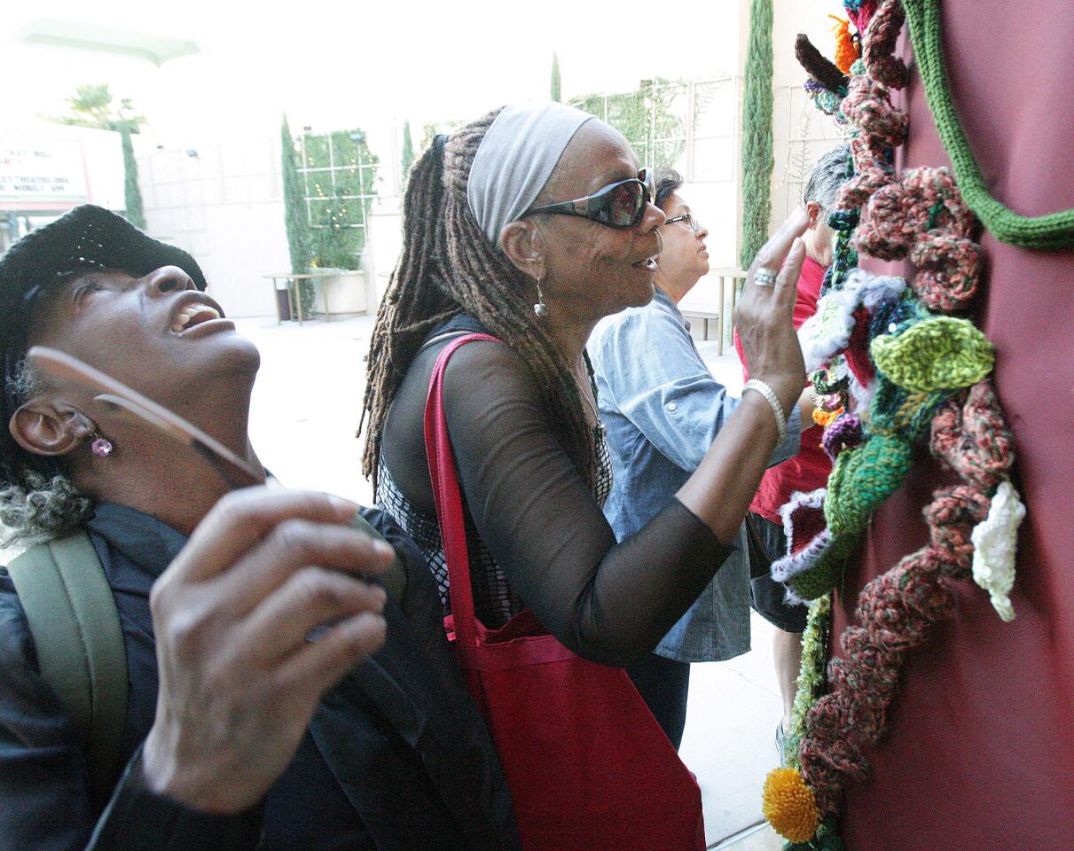 Braille instructor Ester Finney, of Hollywood, looks up a yarn vine covered 21-foot column as her blind student Barbara Ford, of Pasadena touches the texture of the yarn vines at a display called You Are Here, a temporary art series produced by AFTA Productions for the City of Glendale presents Re-Entry, a yarn bombing project by several artists in cooperation with Yarn Bombing Los Angeles at the Alex Theatre in Glendale on Tuesday, October 14, 2015.