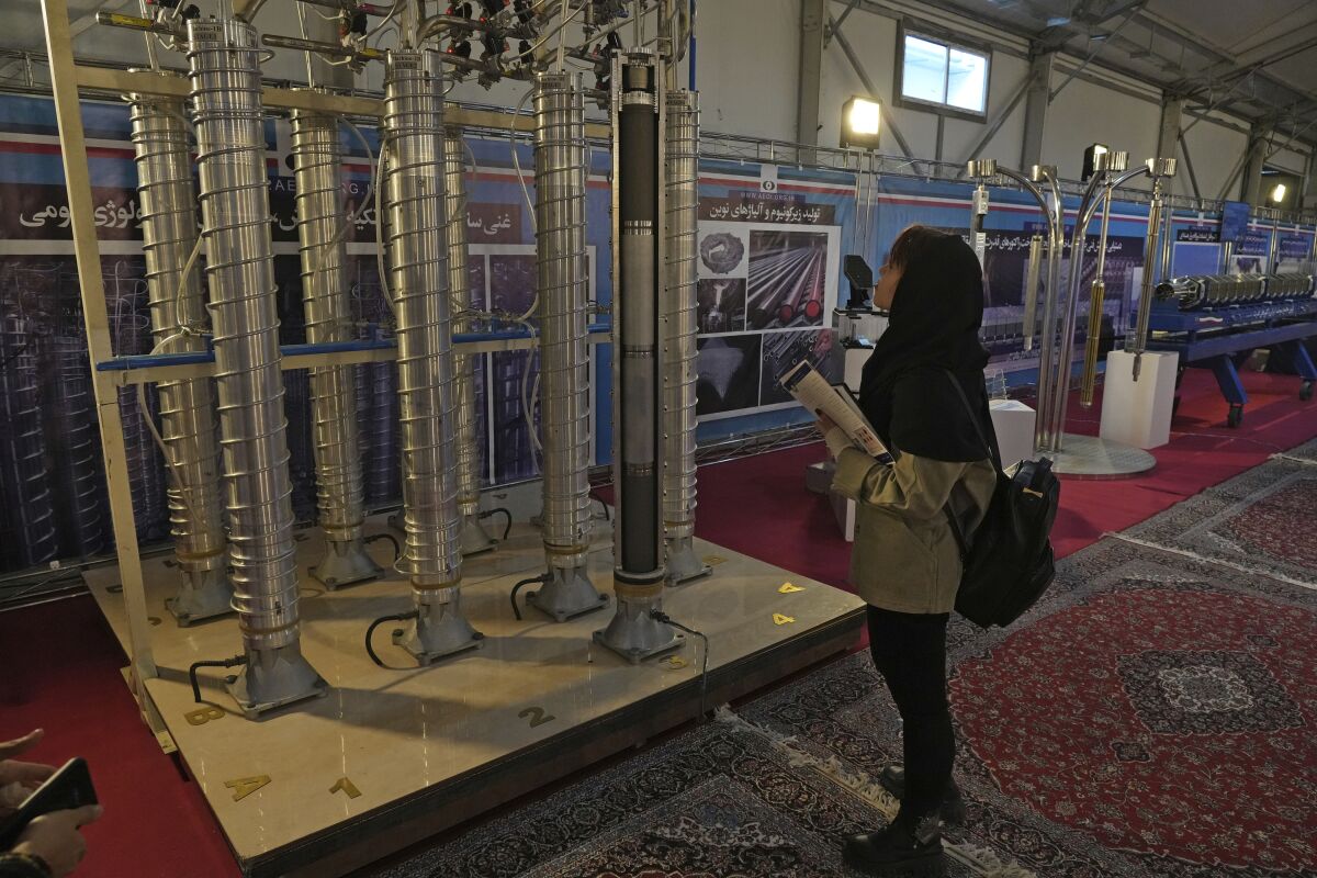 A woman in a dark head covering stands and looks at a group of vertical silver tubes 