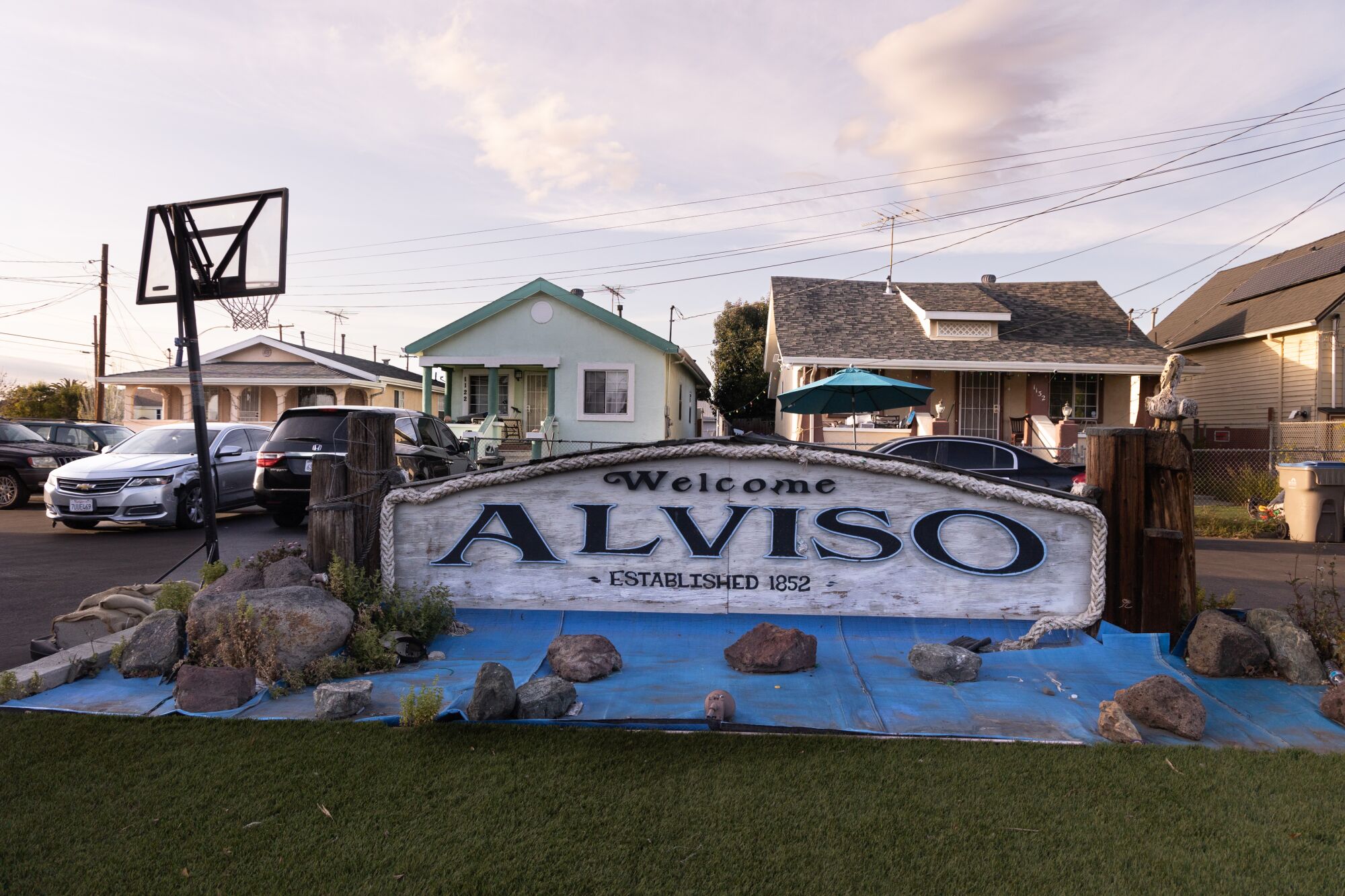 Rocks hold a tarp down in front of a welcome sign in Alviso.