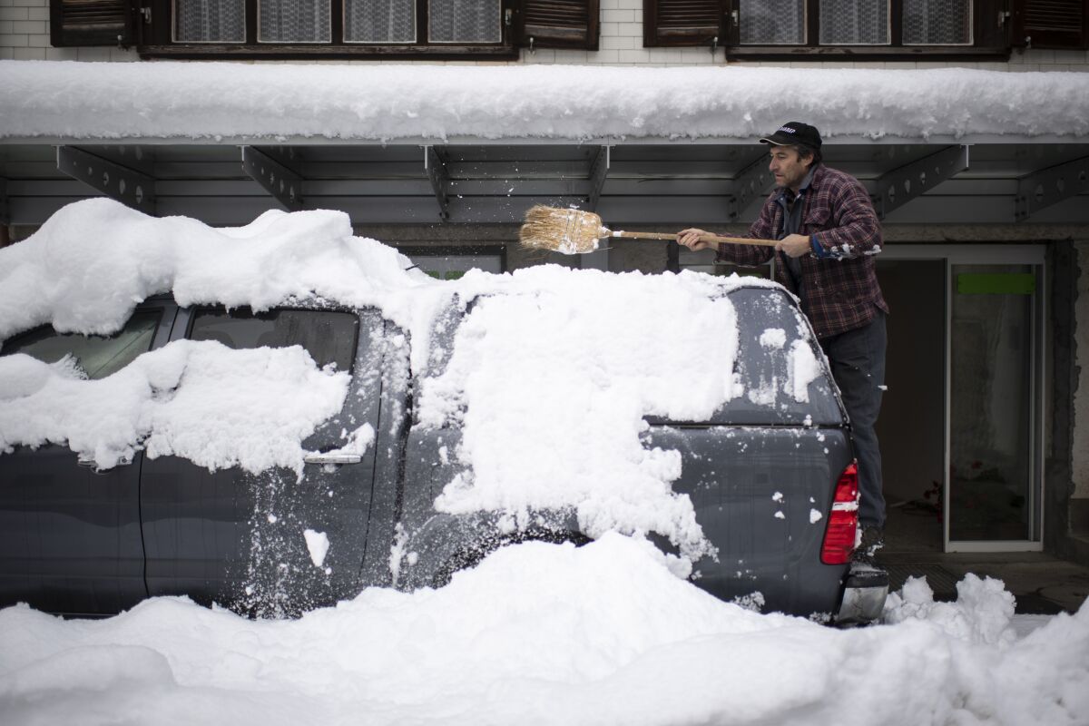 A man cleares his car of snow, on Monday, Dec. 7, 2020, in Valens, Switzerland. Large amounts of snow fell in parts of Switzerland over the weekend. (Gian Ehrenzeller/Keystone via AP)