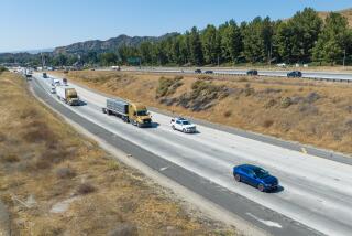 A blue electric car drives on a freeway ahead of other cards including SUVs and trucks.