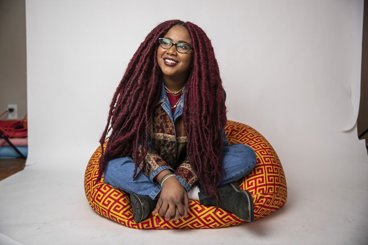 Cinematographer Sade Ndya sits cross-legged on a colorful cushion.  