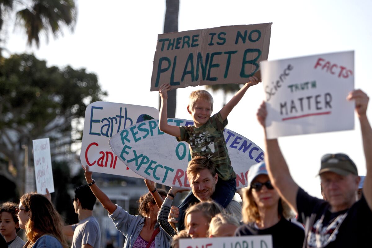 A child sitting on a man's shoulders holds a sign reading "There is no Planet B" at a climate protest.