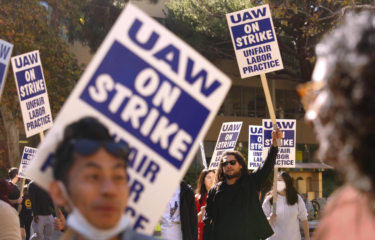 Workers with picket signs that read "UAW on strike: unfair labor practice"