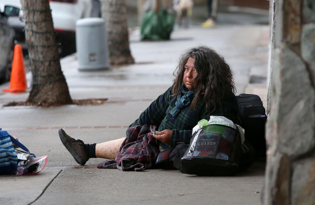 A homeless woman sits on the sidewalk in Laguna Beach.