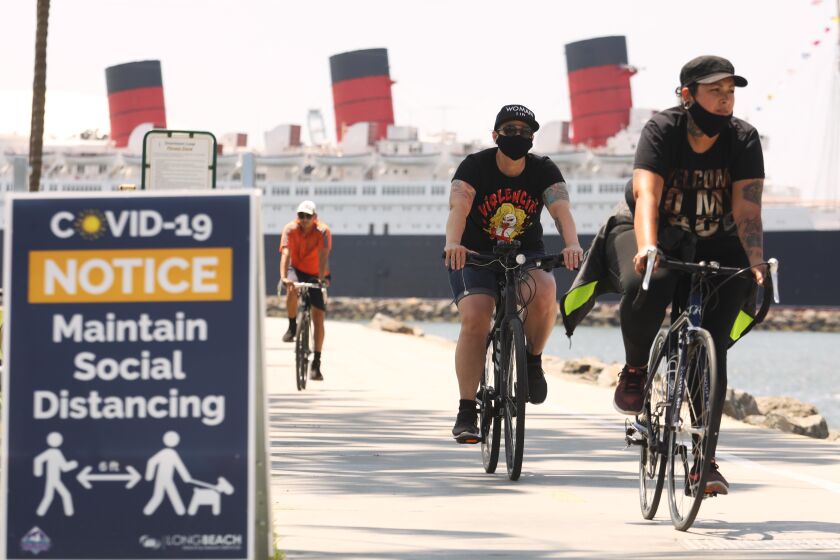 LONG BEACH, CA - MAY 11, 2020 - - Bikers, against a backdrop of the Queen Mary, make their way along pedestrian and beach bike path on the first day that Long Beach reopened the path on Monday May 11, 2020. The city of Long Beach eased a few of its public health restrictions, allowing under certain guidelines the reopening of pedestrian and beach bike paths, tennis centers and courts. Beach bathrooms are also reopening, but the parking lots and beaches still remain closed. (Genaro Molina / Los Angeles Times)