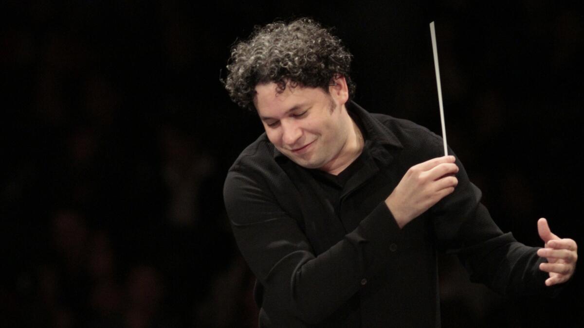 A maestro with curly black hair wearing a black collared shirt and conducting