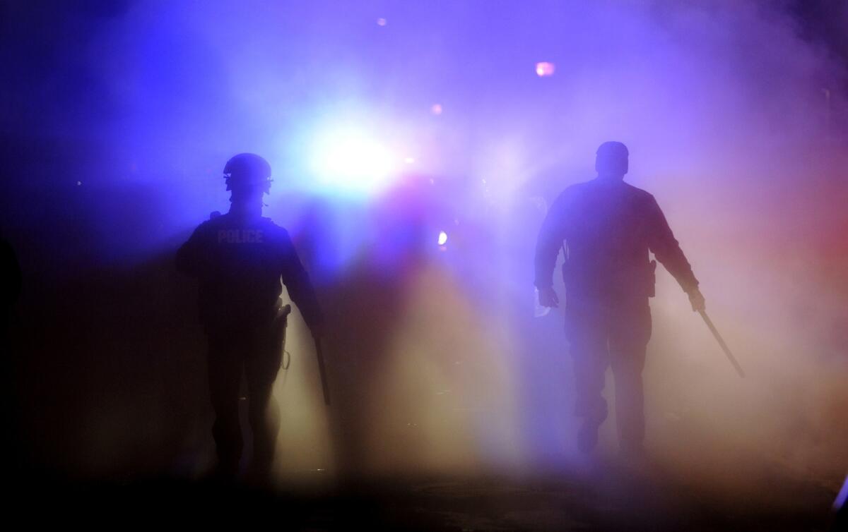 Officers walk through smoke from a burning police vehicle in front of Ferguson City Hall.
