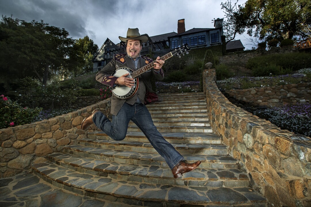 Jan. 25: Jared Gutstadt jumps in the air while holding a banjo in front of stone stairs and a home up a hill