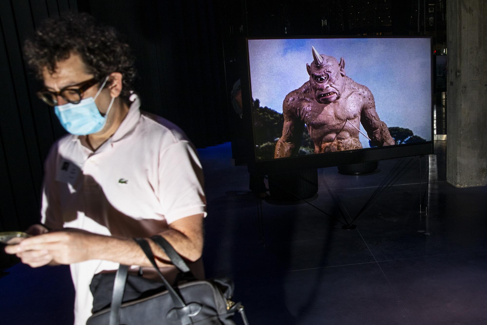 A visitor walks past a screen with a cyclopes on it.