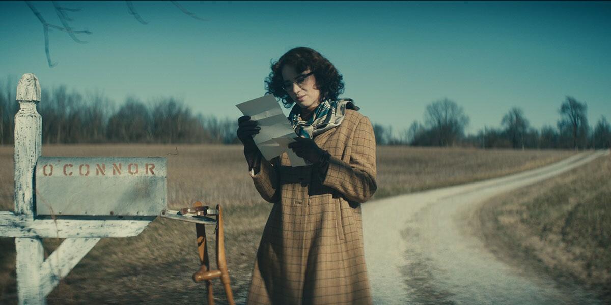 A woman stands in front of her mailbox reading a letter.