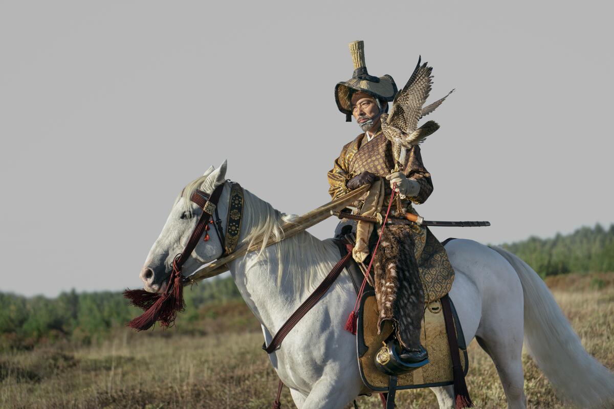 A man in historic Japanese garb holds a bird of prey on his arm as he rides a horse in a scene from “Shōgun.”