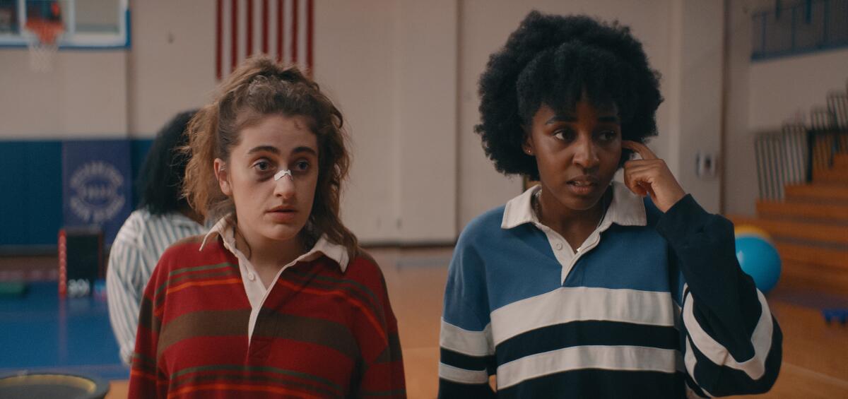 Two high-school girls speak in a gymnasium.