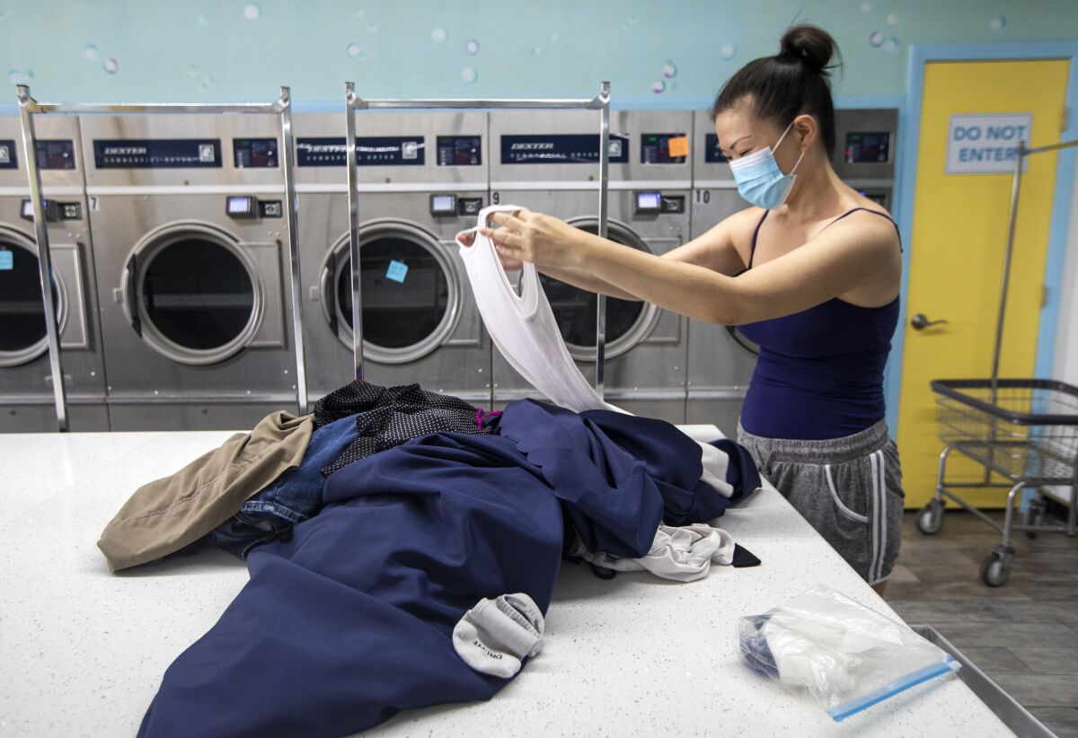 A person wearing a face mark in a coin laundry holds up clothes.