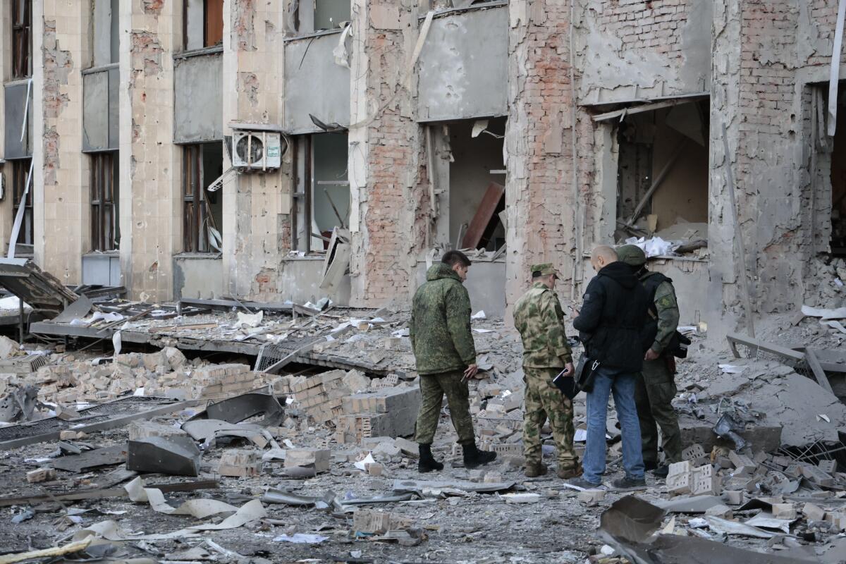 People stand in front of a damaged building with debris around them.