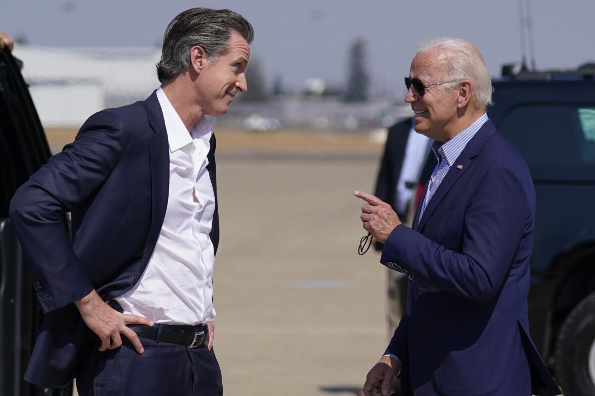 Newsom and Biden stand next to each other in blue suits and speak on an airport tarmac