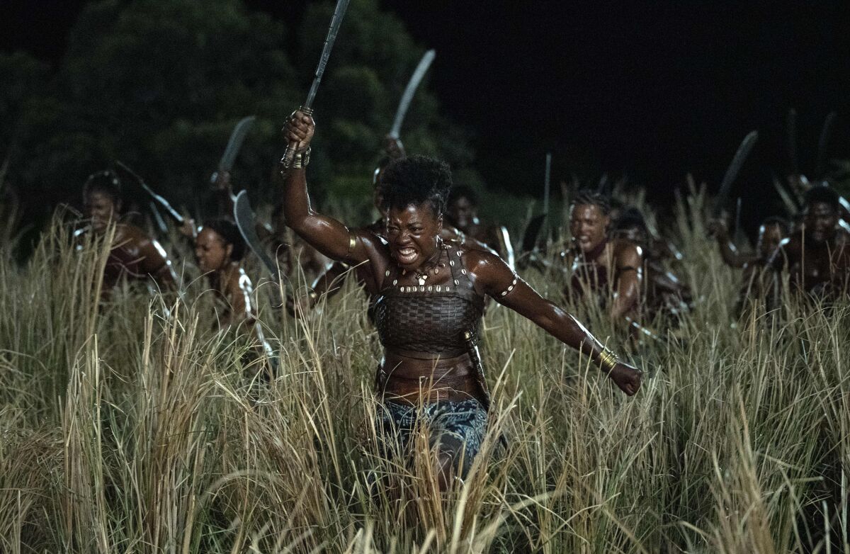 Female warriors charge through tall grass with swords raised in a scene from "The Woman King."