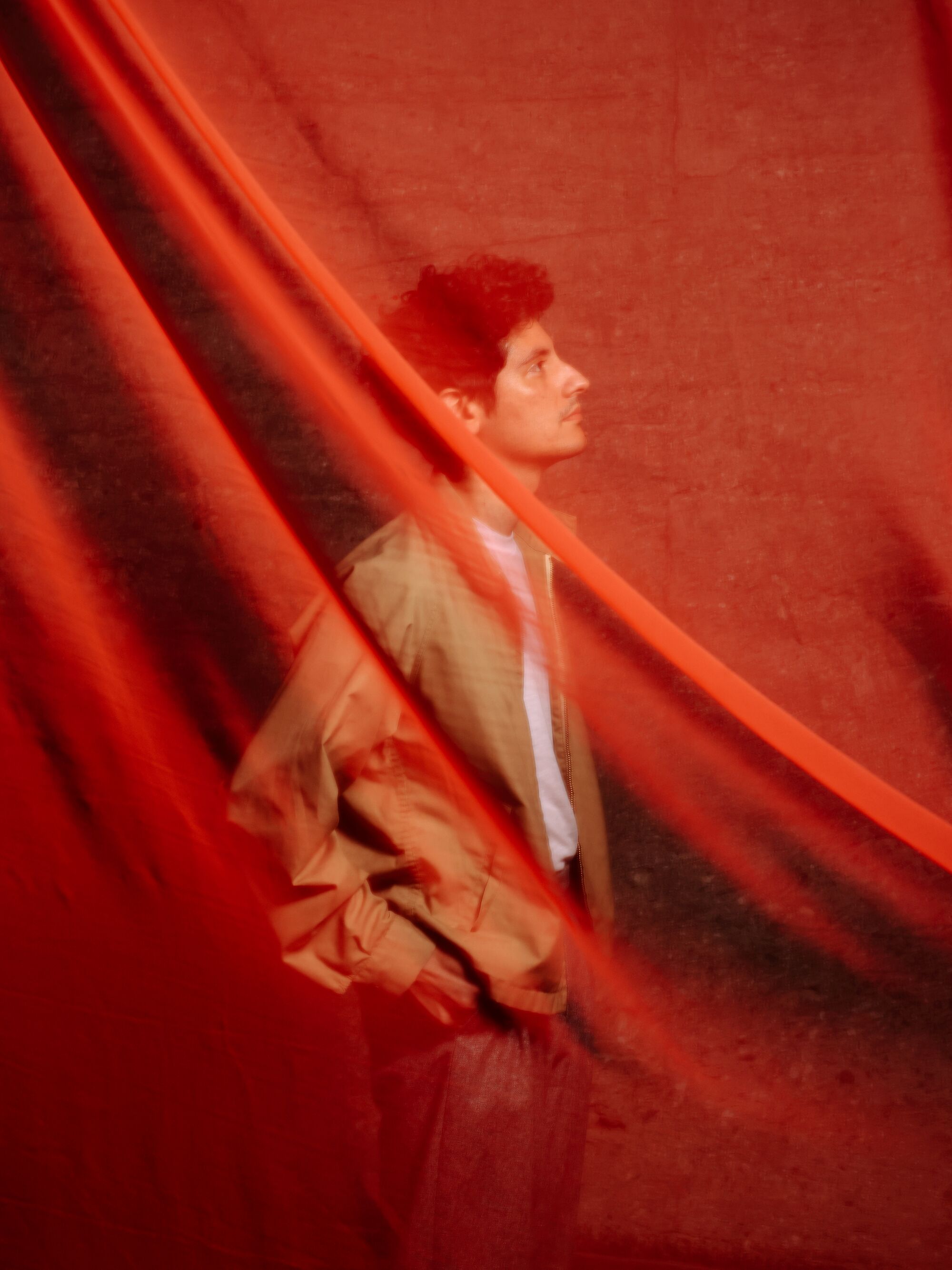 A man stands amid red sheer drapery.