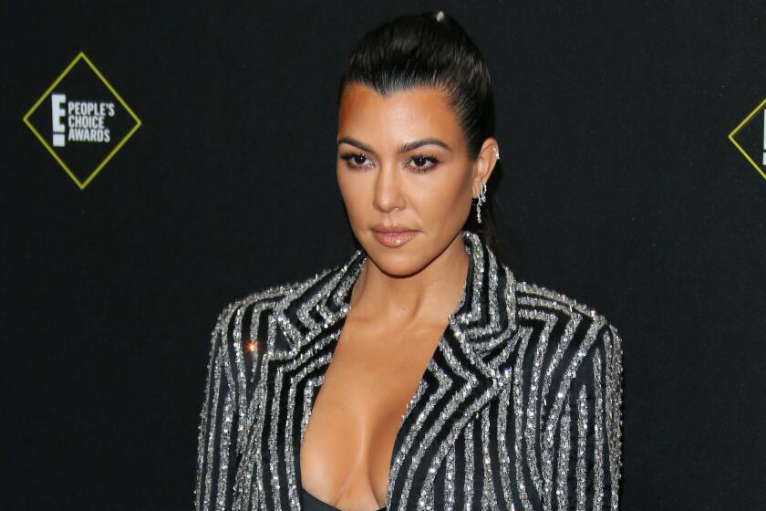 Kourtney Kardashian is posing for photos while wearing a stripped black and glittery blazer with slicked back hair