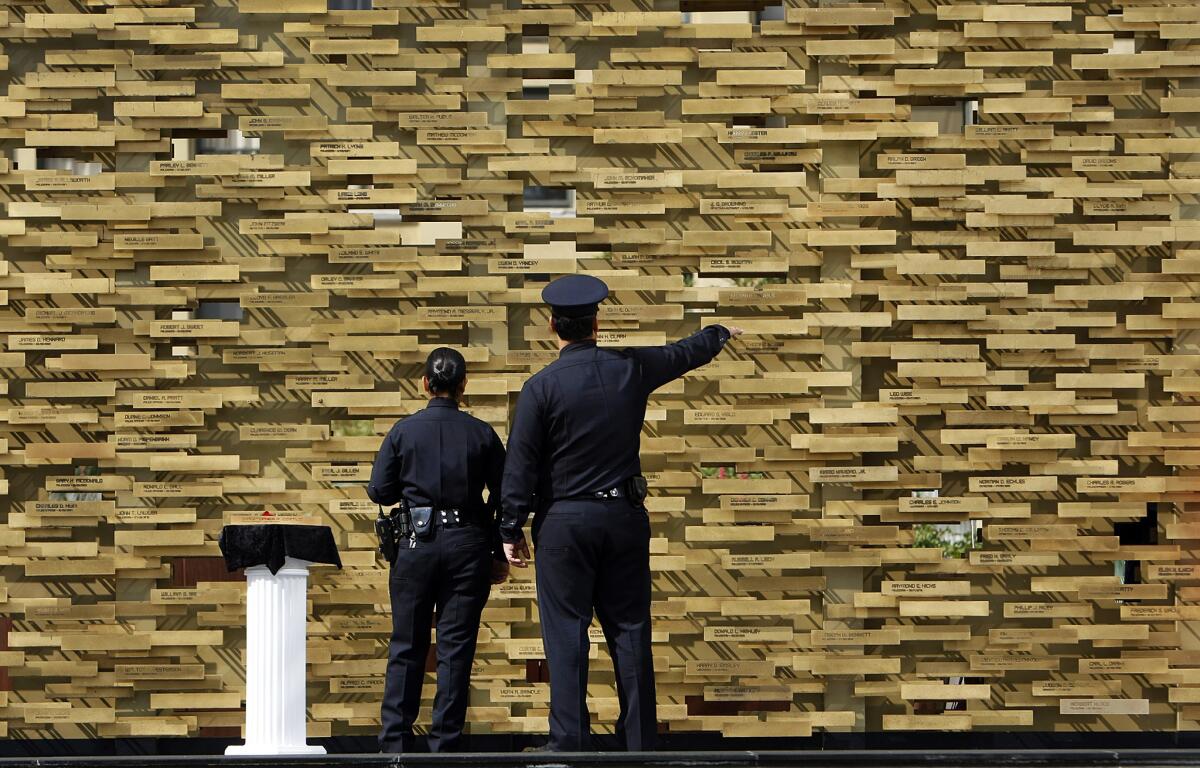 LAPD officers Myra Villafana, left and Paul Cruz take a close look the Los Angeles Police Department Memorial to Fallen Officers, a monument wall located at the downtown headquarters, before the service to honor 207 LAPD officers who've died in the line of duty.