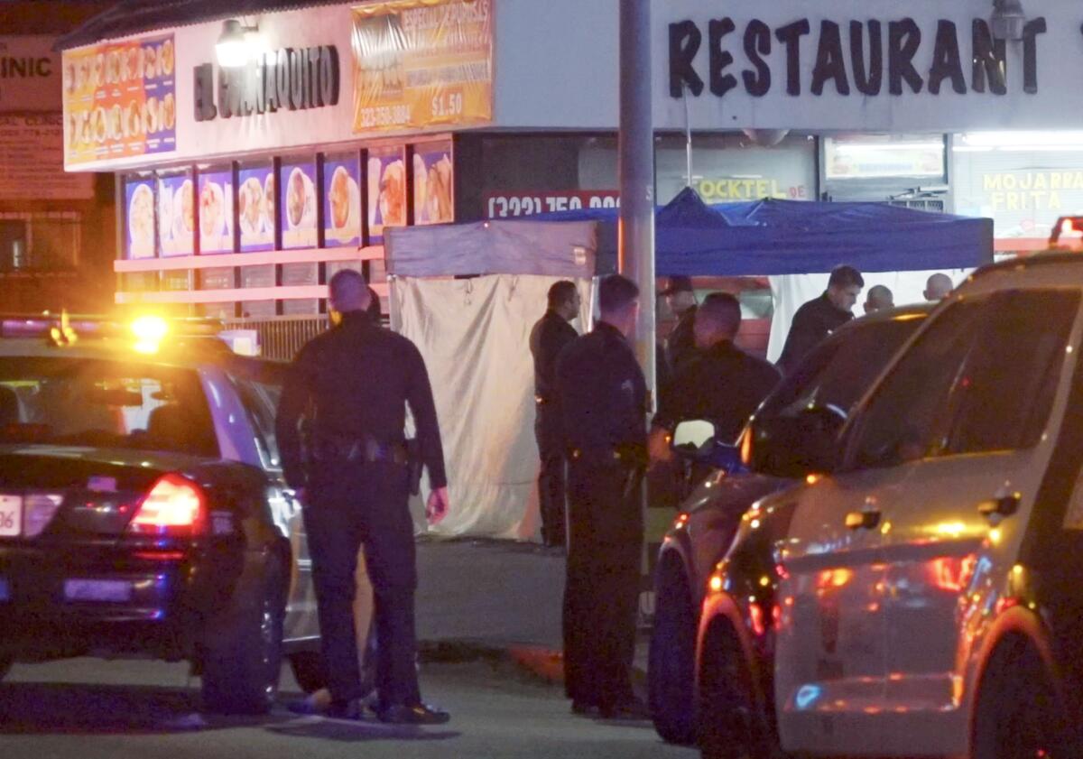 Police officers stand near vehicles outside a restaurant with a canopy set up near it