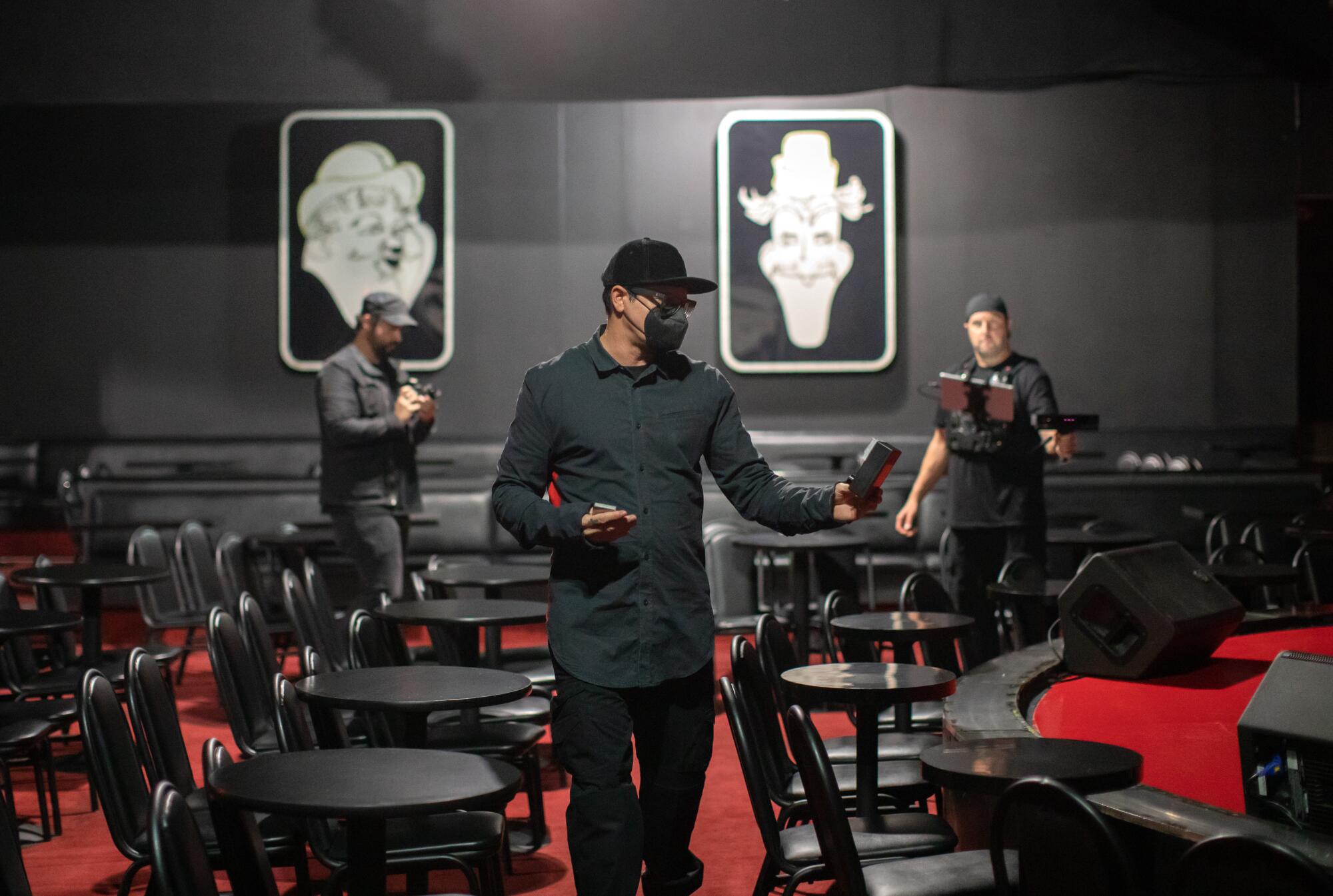 Three men roam among small tables and chairs, scanning it with electronics 