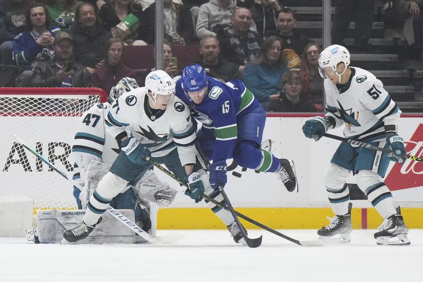 Vancouver Canucks' Sheldon Dries (15) jumps to avoid the puck while being checked by San Jose Sharks' Nikolai Knyzhov (71) in front of goalie James Reimer (47) as Radim Simek (51) watches during the first period of an NHL hockey game in Vancouver, British Columbia, Thursday, March 23, 2023. (Darryl Dyck/The Canadian Press via AP)