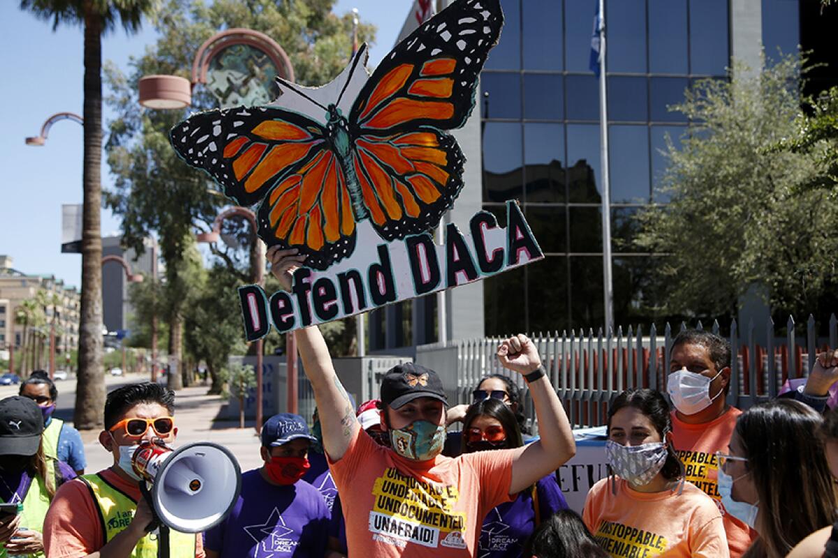 People rally with signs and a megaphone. One large sign with a butterfly says "Defend DACA"