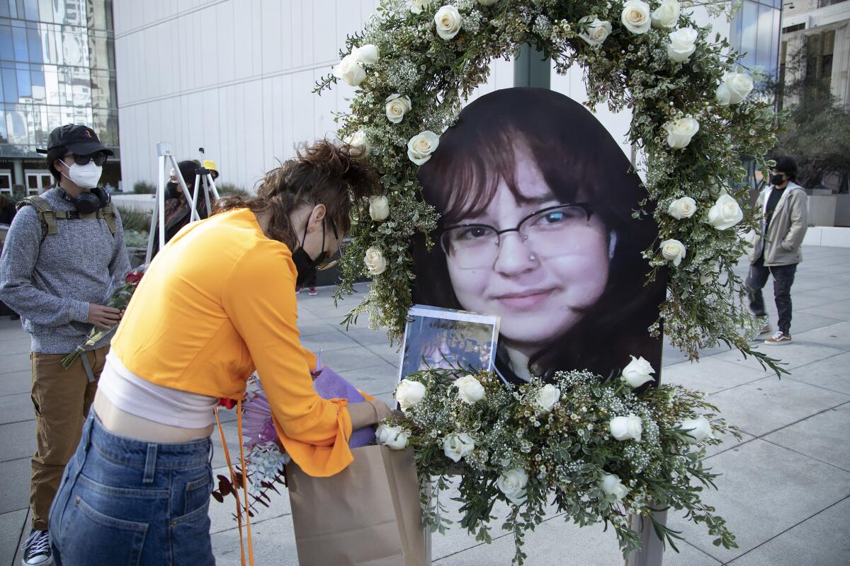 On a sidewalk, people put together a memorial that includes a large picture of a young girl's face and flowers.