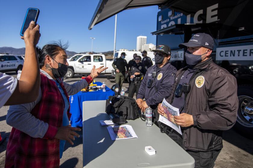 SANTA MONICA, CA - JANUARY 22: Vendors approach police in the parking lot near the Santa Monica Pier on Saturday, Jan. 22, 2022 in Santa Monica, CA. The Santa Monica Police had more than 10 officers staged in the parking lot Saturday. Santa Monica is pushing out unlicensed vendors that sell on the Pier on weekends.A few of the vendors raise their voice and one officer asked them to step back from the table next to the Police vehical. (Francine Orr / Los Angeles Times)