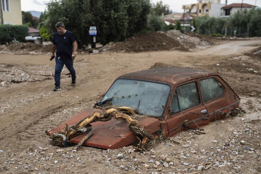 A man walks next to a damaged car after floods in the town of Agria near the city of Volos, Greece, Thursday, Sept. 28, 2023. A second powerful storm in less than a month hammered parts of central Greece Thursday, sweeping away roads, smashing bridges and flooding thousands of homes. (AP Photo/Petros Giannakouris)